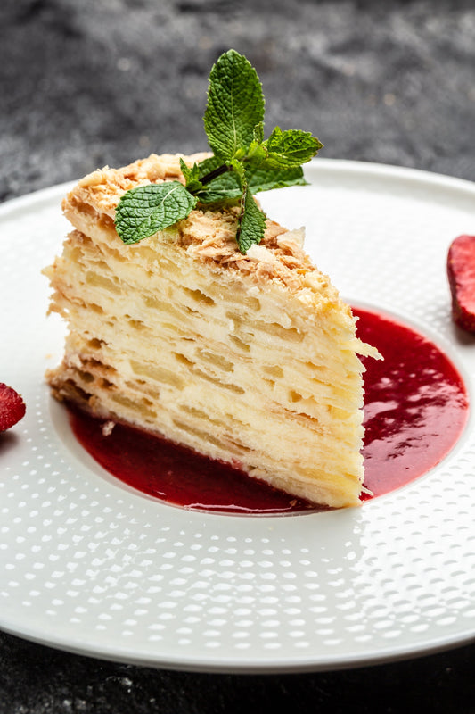 Gluten Free Apple Layer Cake showing multiple layers of apple and cake on top of a raspberry puree and fresh mint leaves on top. All on top of a white plate.
