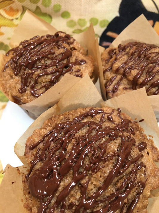 Three golden mile high muffins drizzled with chocolate topping.
