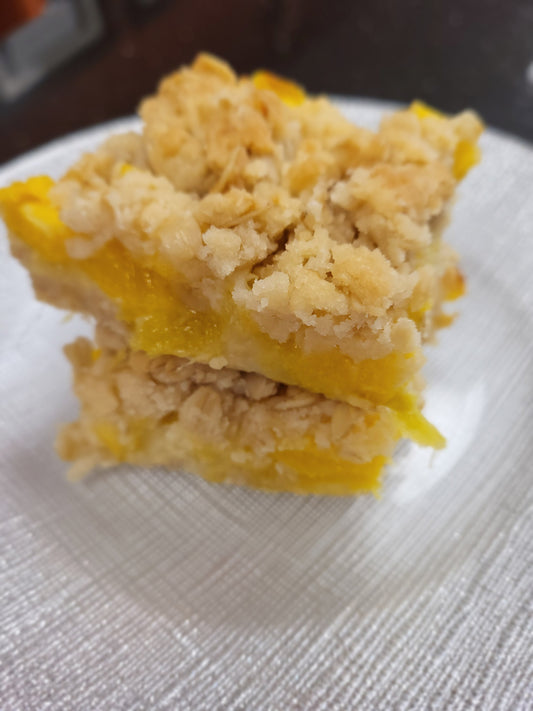Two gluten free mango bars with crumble crust and topping on a silver-white plate.