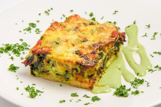 Scrippelle (crepe) lasagna with mushrooms and spinach. on a white plate with green sauce and chopped green parsley sprinkled around scrippelle