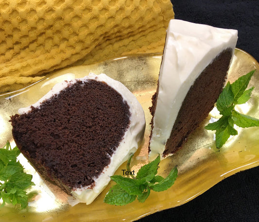 Deep chocolate cake covered with a fluffy white topping on a gold dish and green fresh mint leaves placed around with black and gold background.