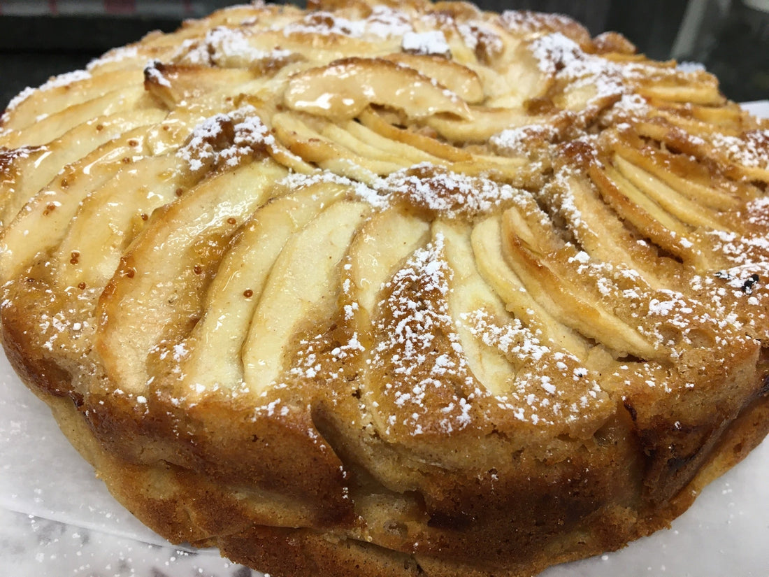A lovely gluten free apple cake dusted with powdered sugar on a white base.