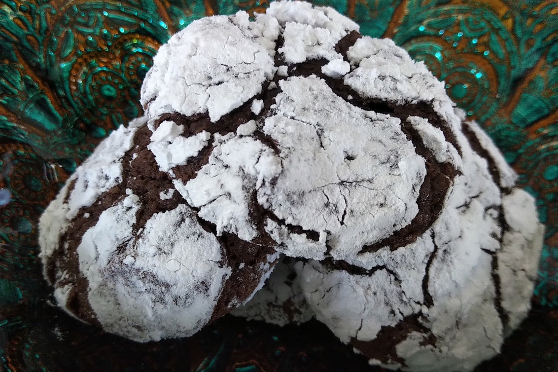 three dark chocolate cookies with icing sugar coating sitting on green dish.