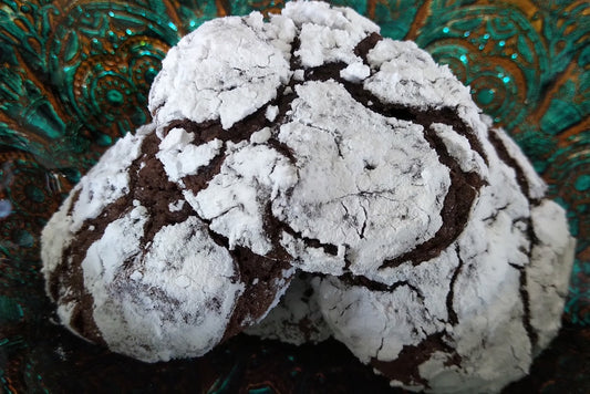 three dark chocolate cookies with icing sugar coating sitting on green dish.