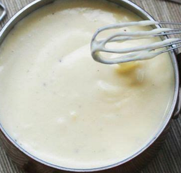 Creamy bechamel sauce in a pot, with a whisk placed over a portion of the pot.