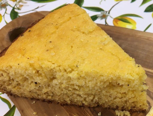 Golden slice of cornbread on top of a wooden platter on a lemon patterned table cloth.