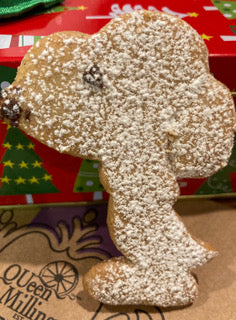 Snoopy character cookie dusted in icing sugar standing against a red Christmas box