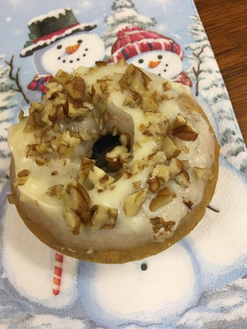 Gluten free old fashion donut topped with icing and nuts on a snowman napkin