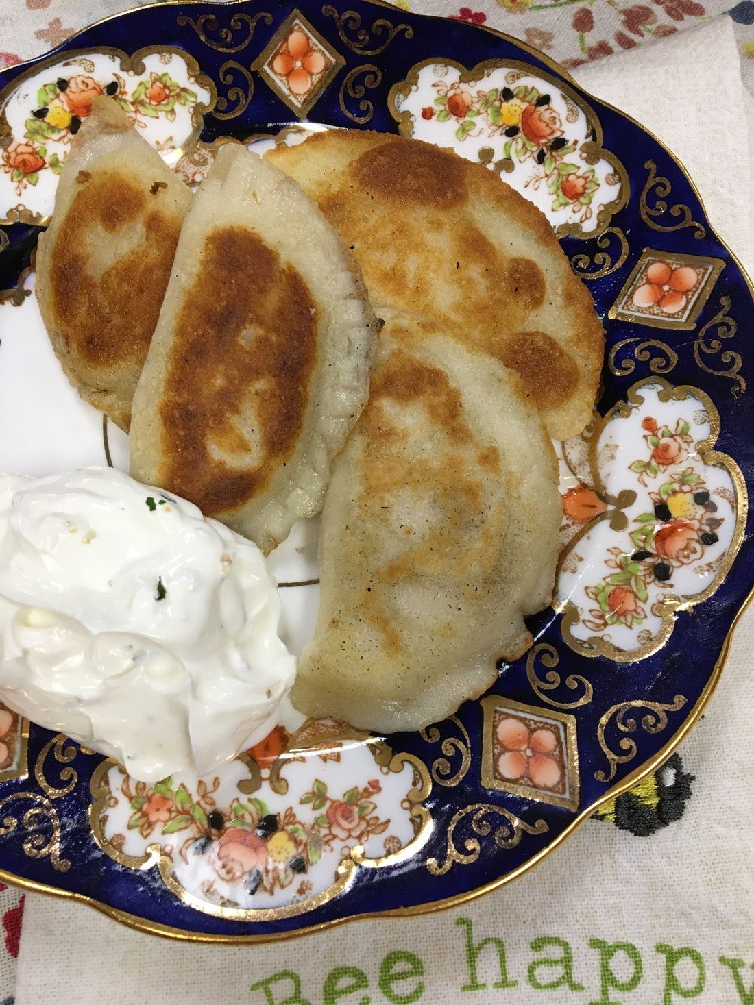 A blue and multi colour plate with 4 golden gluten free pierogi and a side of dollop of sour cream.