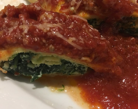 A spinach and cheese stuffed cannelloni on a white plate topped with fresh tomato sauce.