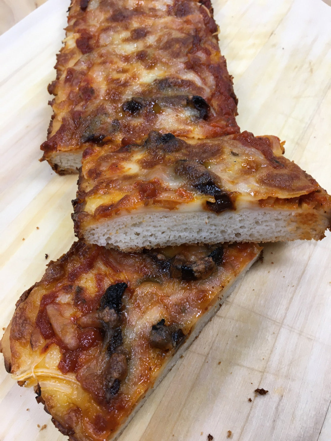 slices of gluten free pizza on a wooden cutting board.