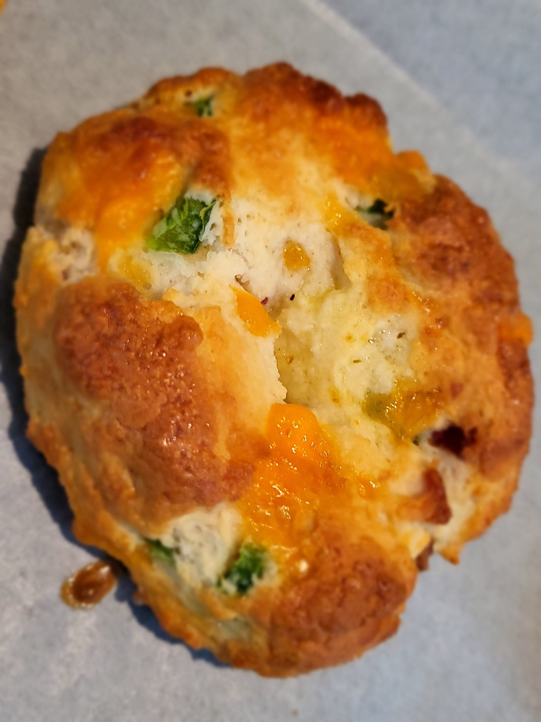 Baked bagel with melted cheddar cheese and diced jalapeno peppers on a piece of parchment paper.