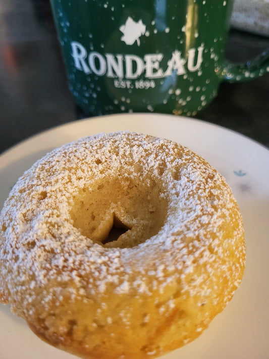 A single baked gluten free old fashion donut on a white plate, with a green and white Rondeau cup in the background.
