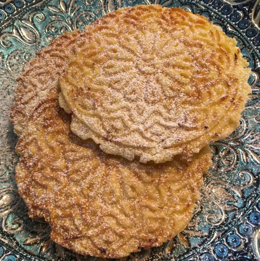 crispy pizzelle cookies dusted with icing sugar on a blue plate.