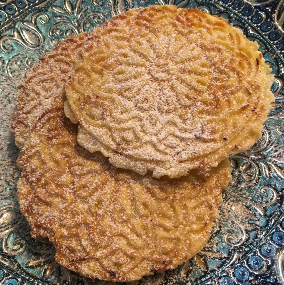 crispy pizzelle cookies dusted with icing sugar on a blue plate.