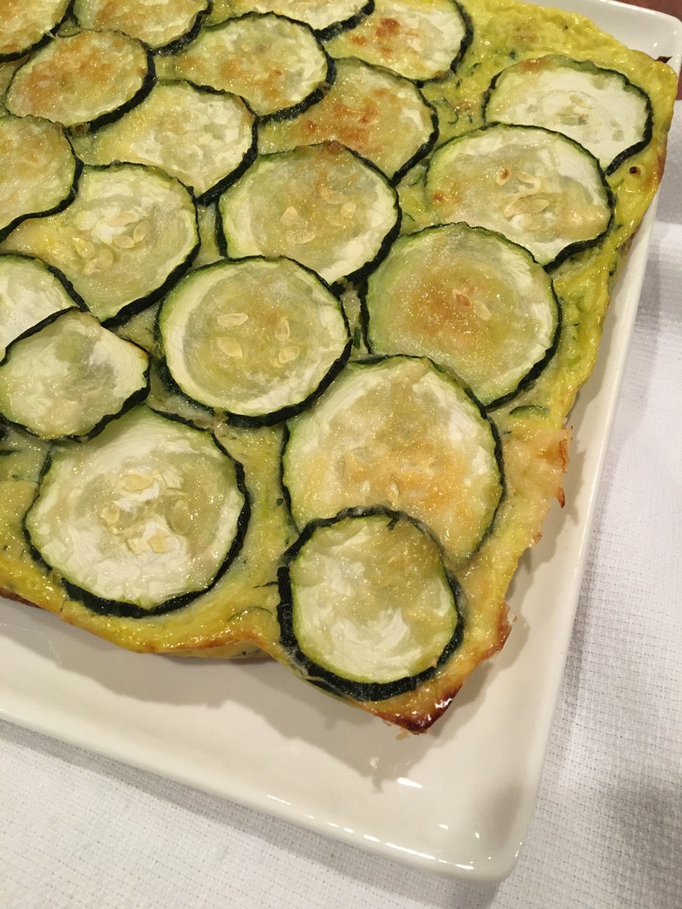 White plate with zucchini topped gluten free base.  Baked golden
